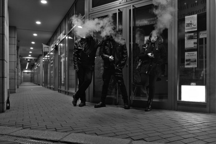 Zwei Männer und eine Frau stehen nachts in einer Ladenpassage und rauchen