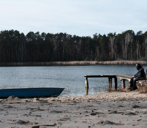 ein boot liegt ruhig am strand und auf dem steeg sitzen zwei menschen