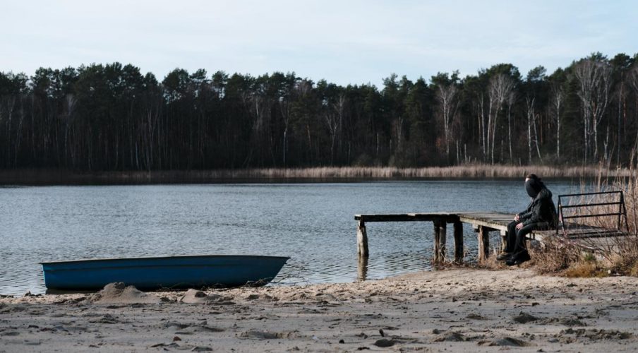 ein boot liegt ruhig am strand und auf dem steeg sitzen zwei menschen